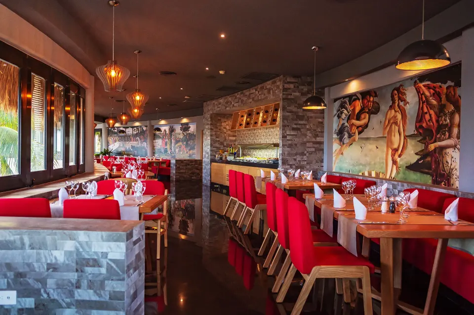 Indoor restaurant with red seating and classical mural at The Reef Playacar Beach Resort & Spa