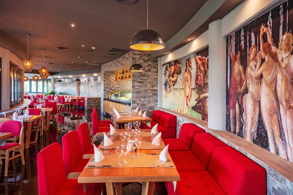 Cozy restaurant seating with red banquettes and artwork at The Reef Playacar Beach Resort & Spa