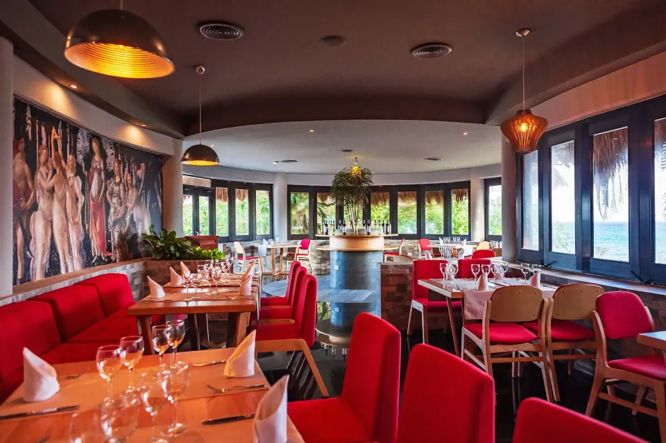 Curved dining room with red chairs and panoramic windows at The Reef Playacar Beach Resort & Spa