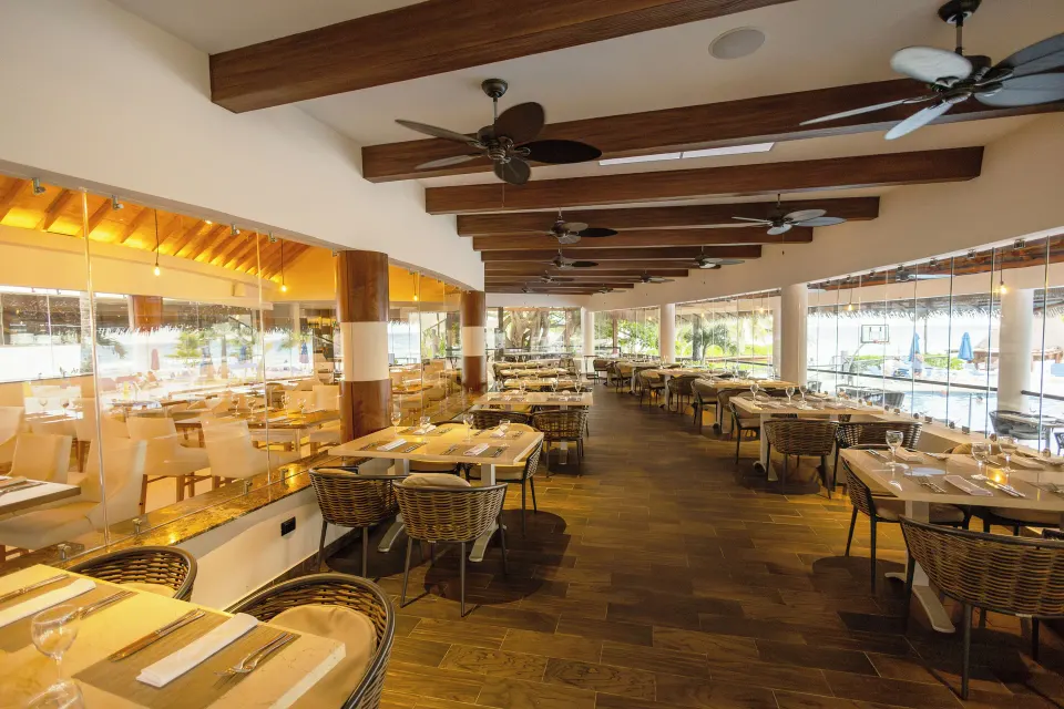 Long buffet-style dining room with wicker chairs and ceiling fans at The Reef Playacar Beach Resort & Spa