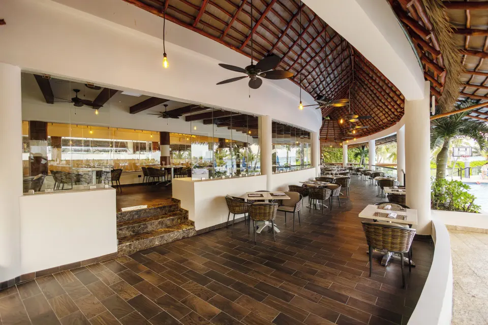 Covered outdoor terrace seating with round tables at The Reef Playacar Beach Resort & Spa