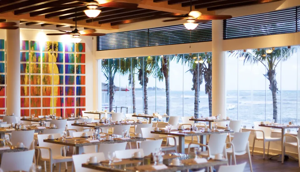 Bright ocean-view dining room with tables and colorful wall art at The Reef Playacar Beach Resort & Spa