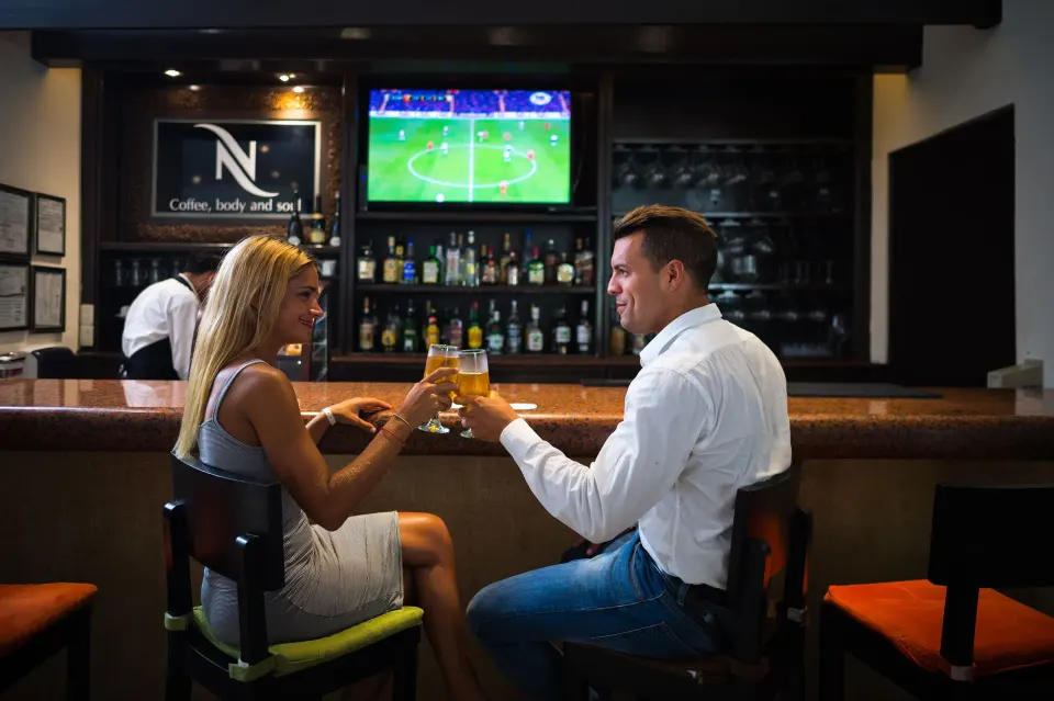 Couple toasting drinks at a sports bar inside The Reef Playacar Beach Resort & Spa