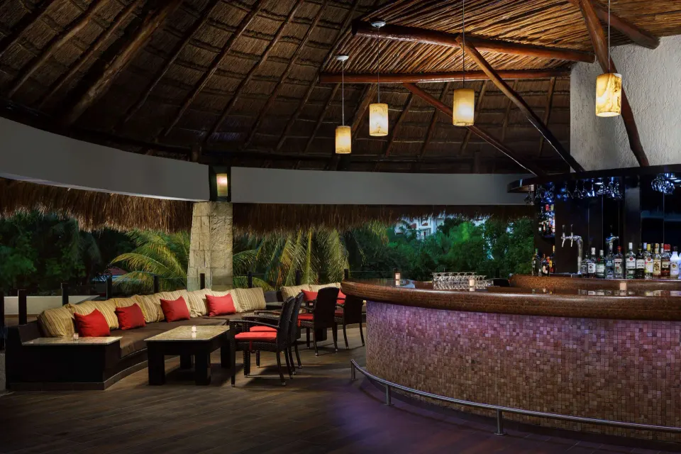 Thatched-roof bar interior with curved counter and lounge seating at The Reef Playacar Beach Resort & Spa