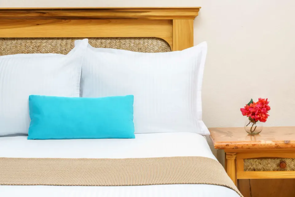 Close-up of bed pillows and bedside table with flower in a Superior Room at The Reef Playacar Beach Resort & Spa