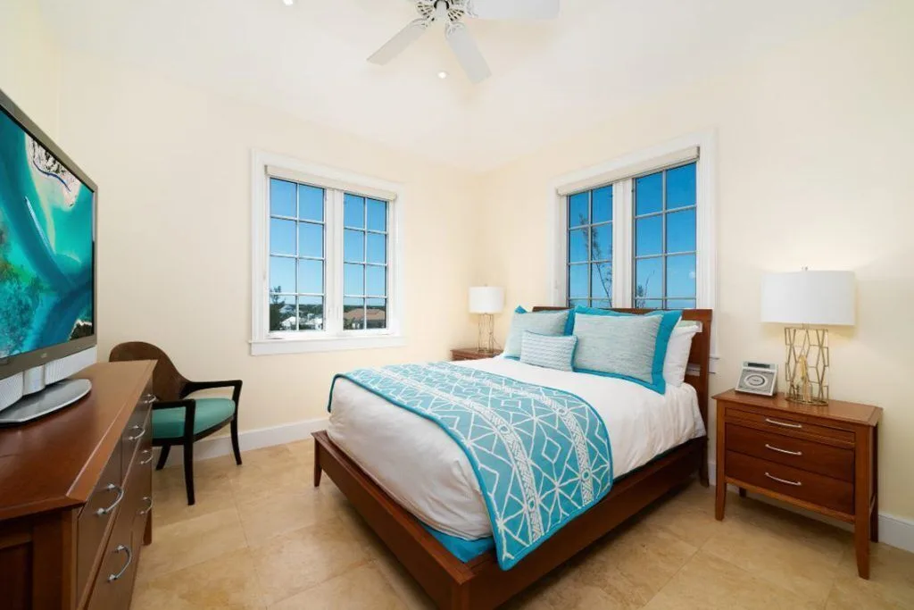 Bedroom with a wood-framed bed, turquoise bedding, windows and TV at The Regent Grand.