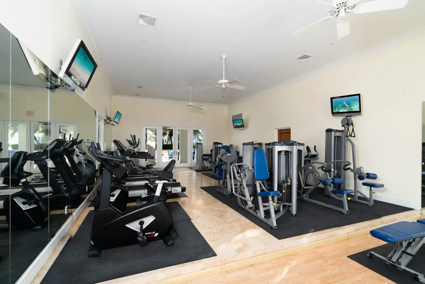 Fitness room with cardio machines, weight equipment, mirrors, and TVs at The Regent Grand.