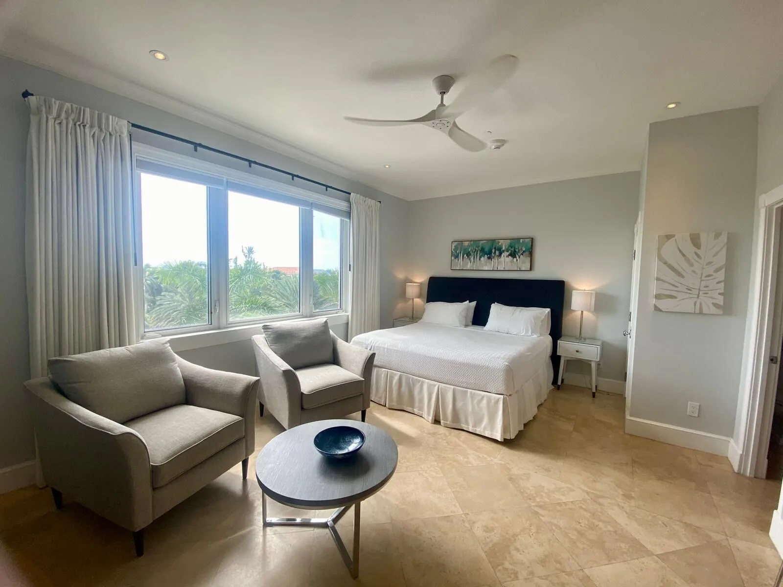 Guest room with a bed, two armchairs, coffee table and large windows at The Regent Grand.