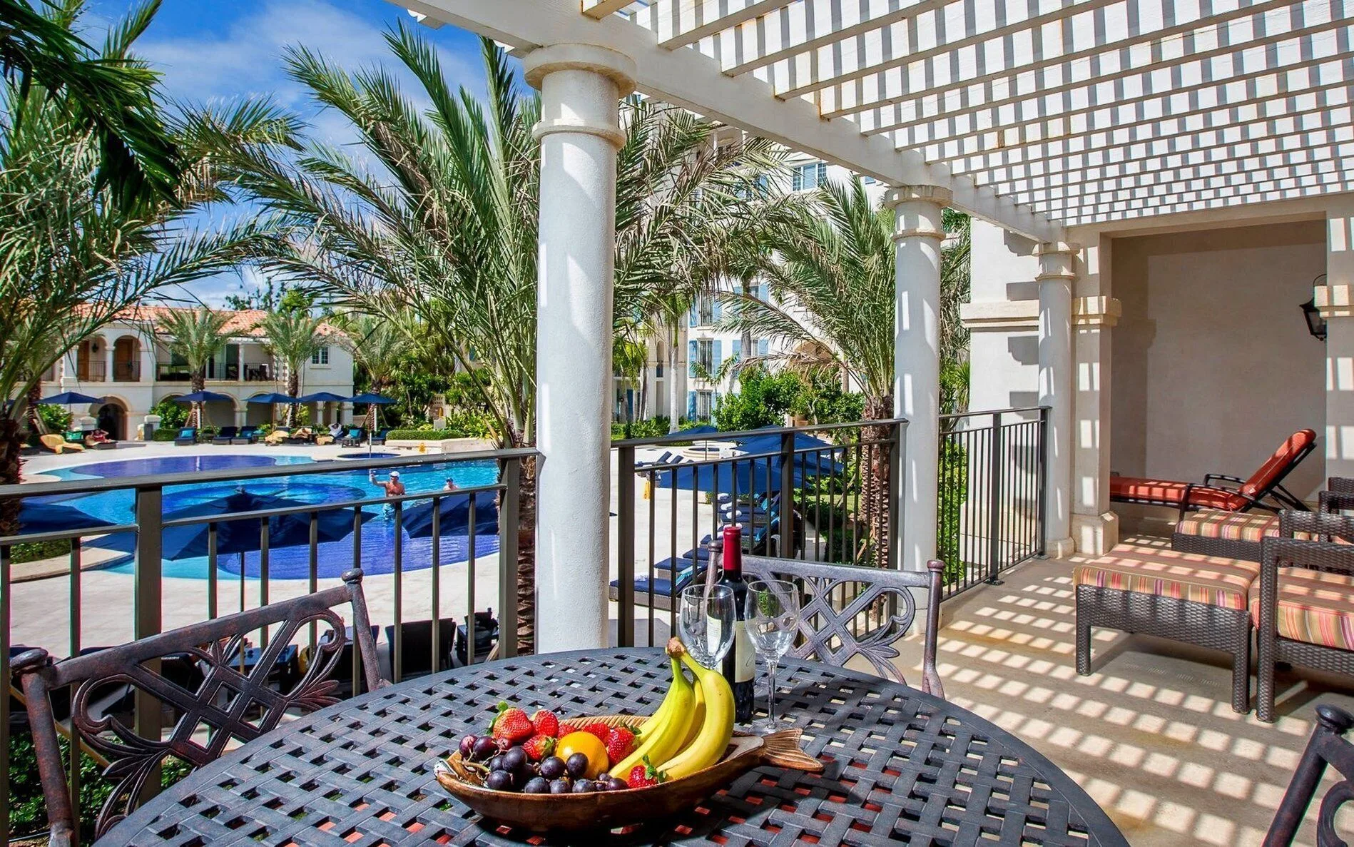 Pool-view terrace with dining table, fruit, wine, and lounge chairs at The Regent Grand.