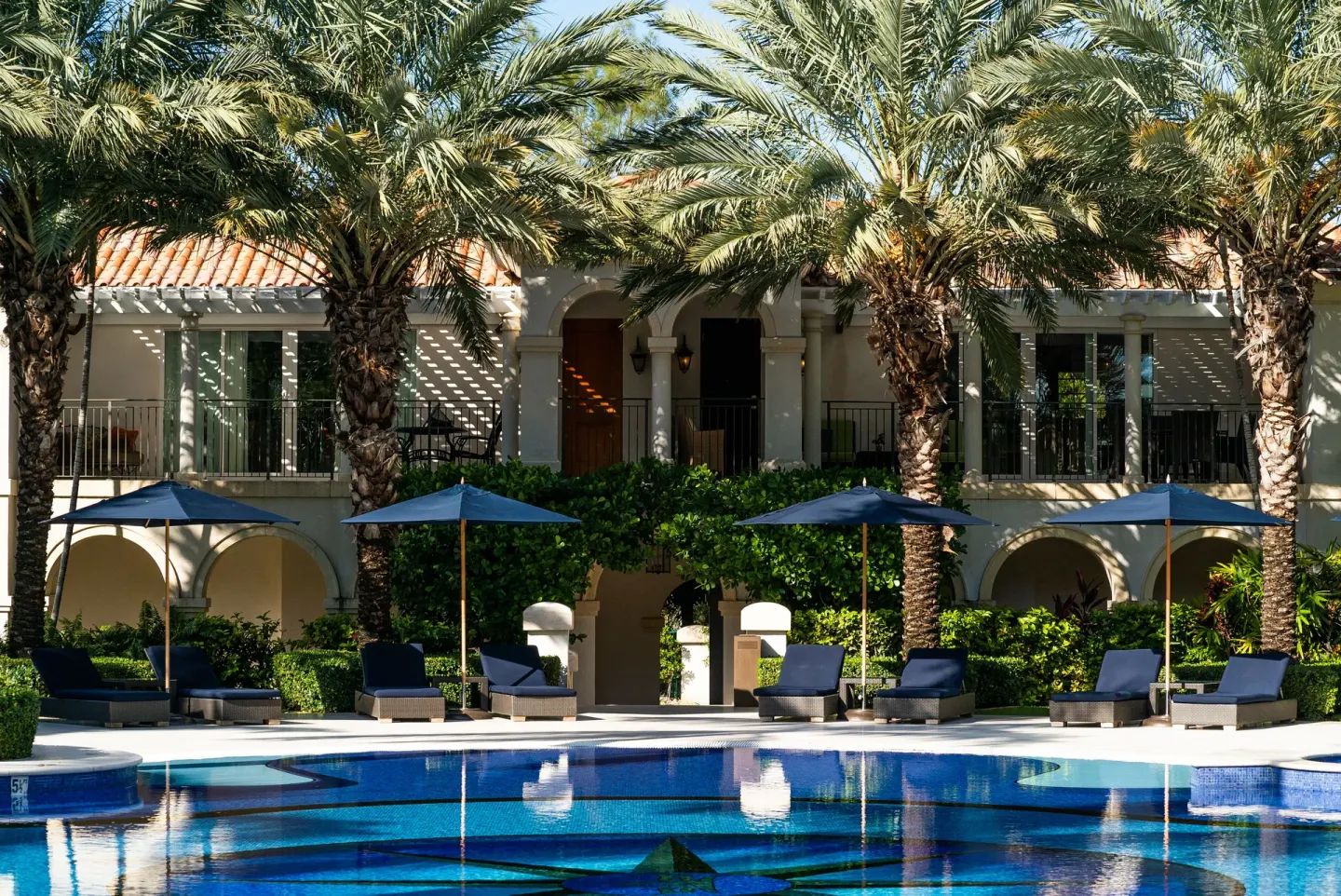 Poolside loungers and umbrellas beside palm trees at The Regent Grand.