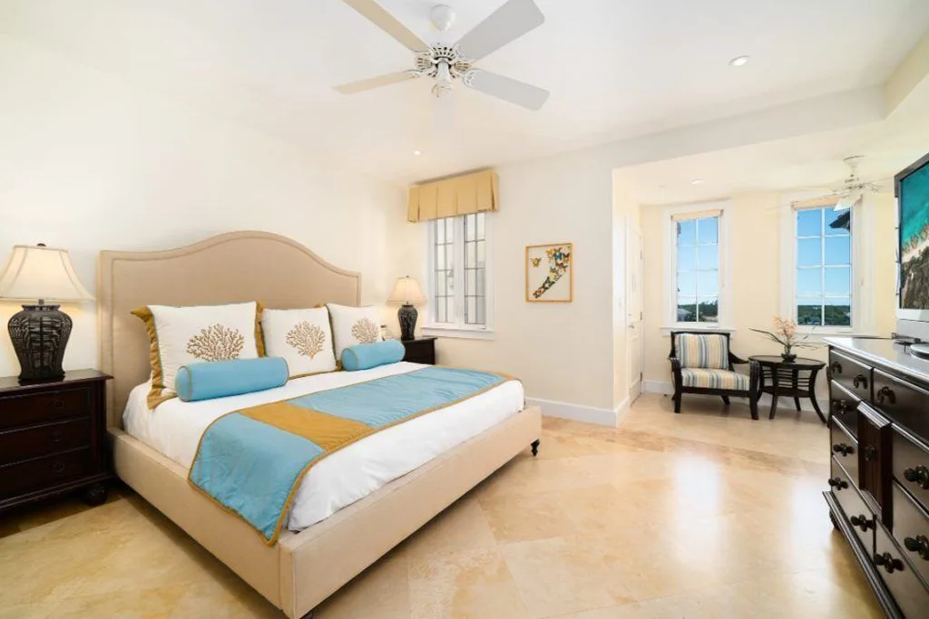 Spacious bedroom with a cream bed, blue accents, sitting nook and dresser at The Regent Grand.