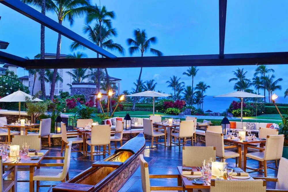 Open-air dining setup with tables and ocean glimpse at The Resort at Kapalua Bay, Maui