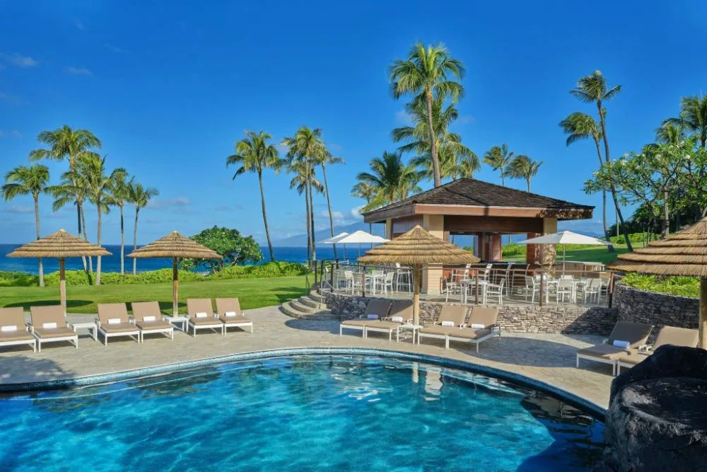 Poolside bar and lounge chairs with ocean and palm trees at The Resort at Kapalua Bay, Maui
