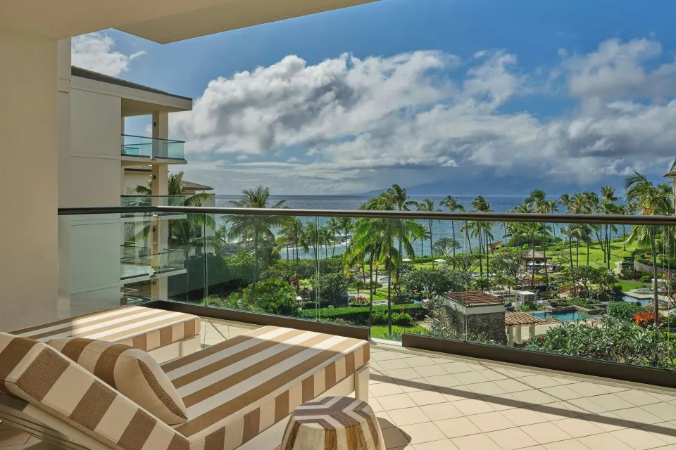 Ocean-view lanai with striped lounge chairs overlooking palm trees and the sea at The Resort at Kapalua Bay, Maui