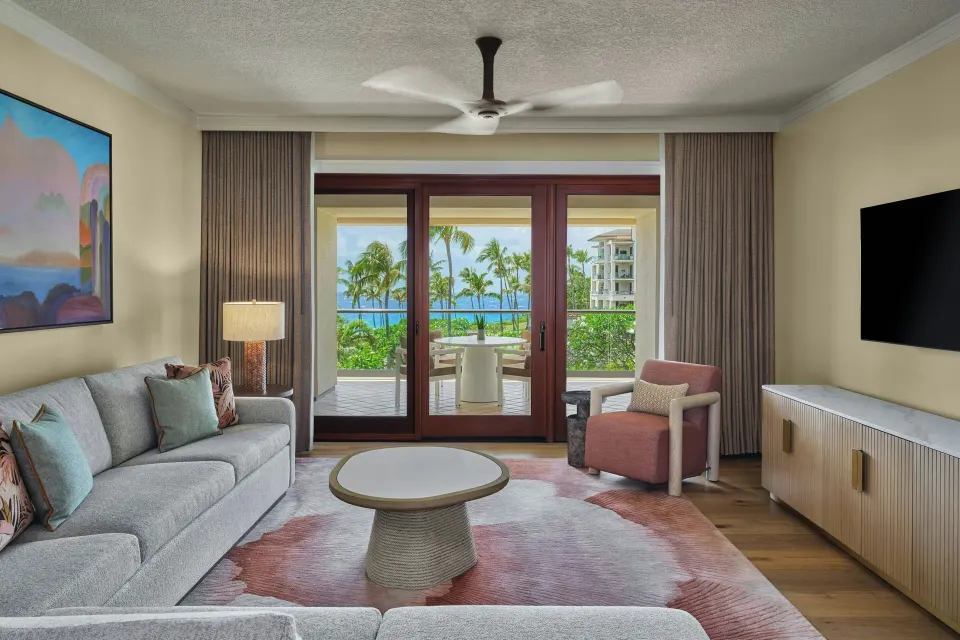 Living room with sofa facing glass doors to the lanai and ocean view at The Resort at Kapalua Bay, Maui
