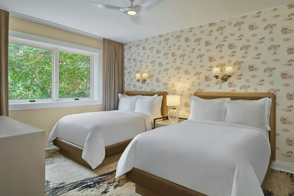 Two double beds with patterned wallpaper and a window view in a residence at The Resort at Kapalua Bay, Maui