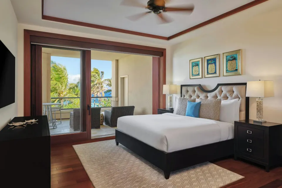 King bedroom opening onto balcony with outdoor chairs and partial ocean view at The Resort at Kapalua Bay, Maui
