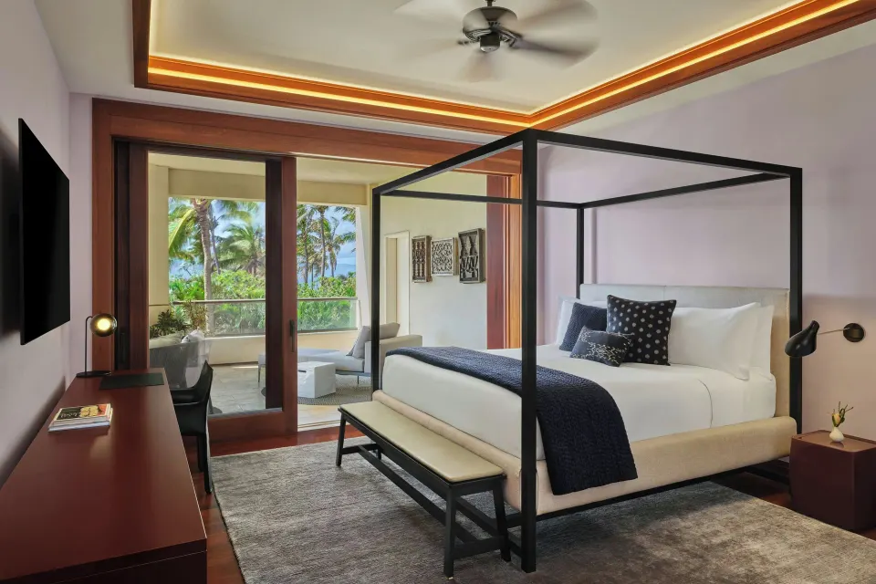 King bed with four-poster frame in a bedroom opening to a balcony with ocean glimpses at The Resort at Kapalua Bay, Maui