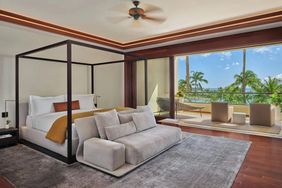 Master bedroom with four-poster bed and balcony view of palms and ocean at The Resort at Kapalua Bay, Maui