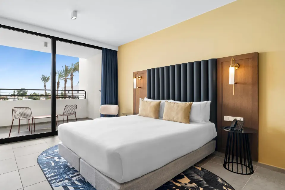 King bed beside sliding balcony doors in a Deluxe Ocean View room at The Rif at Mangrove Beach Corendon Curacao, Curio.