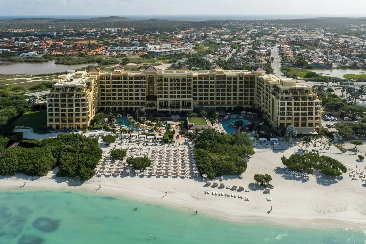 Aerial beachfront view of The Ritz-Carlton, Aruba with pools and palapas.