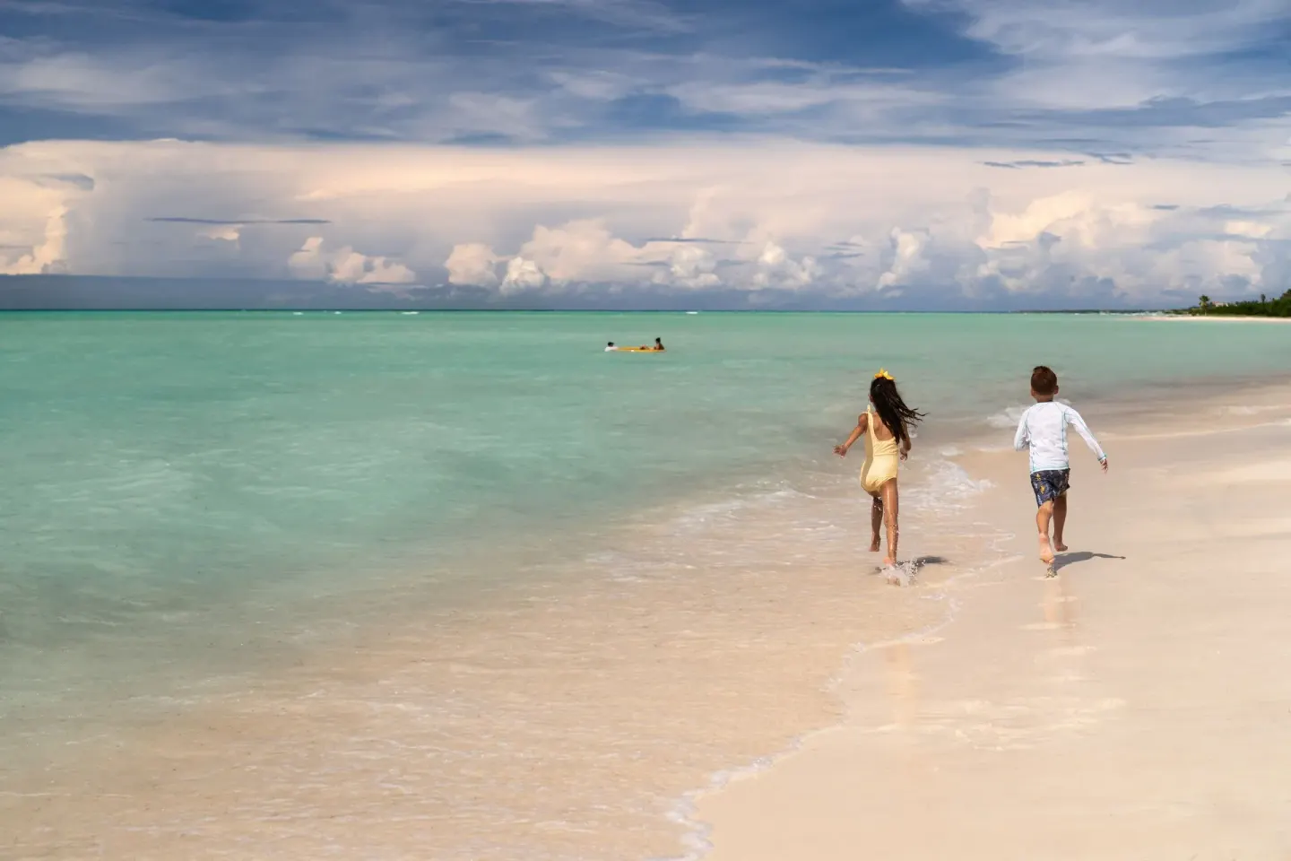 Children run along the shoreline beside clear water at The Ritz-Carlton, Aruba.