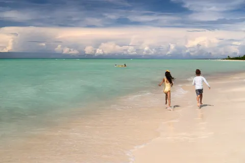 Children run along the shoreline beside clear water at The Ritz-Carlton, Aruba.