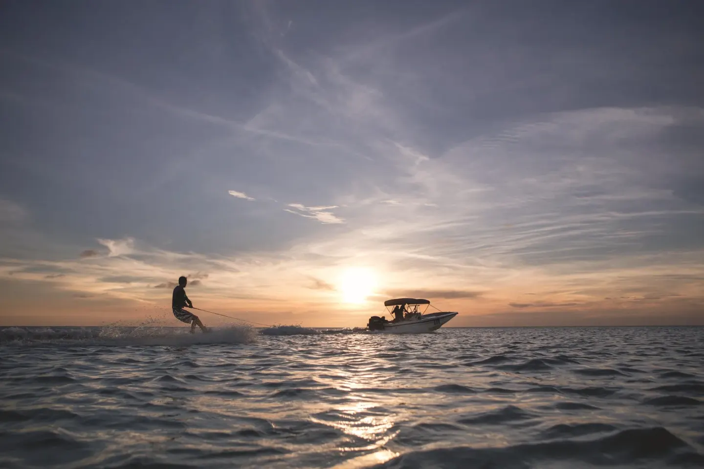 A waterskier and boat cross the ocean at sunset near The Ritz-Carlton, Aruba.