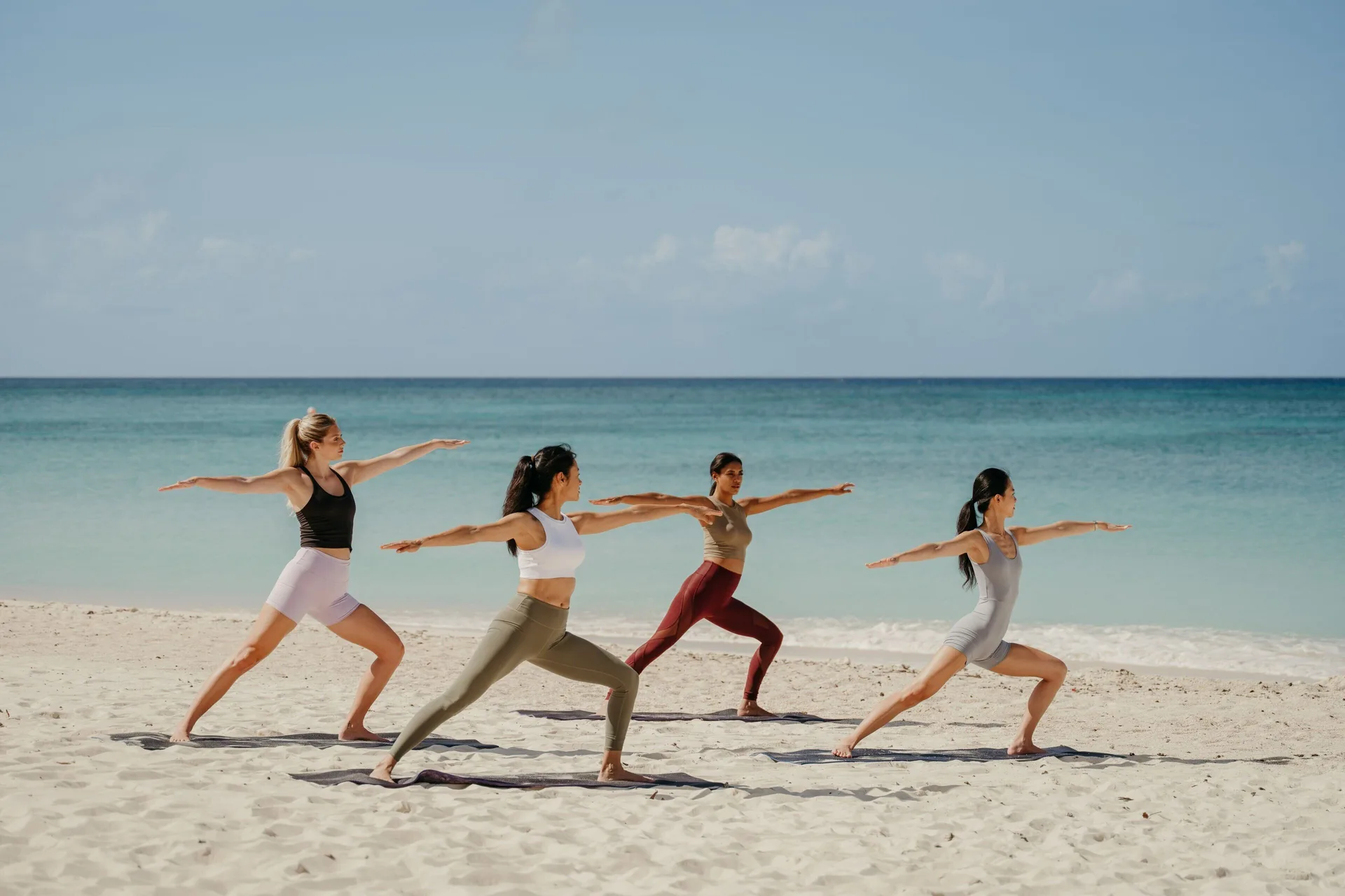 Four people practice yoga on the beach at The Ritz-Carlton, Grand Cayman.
