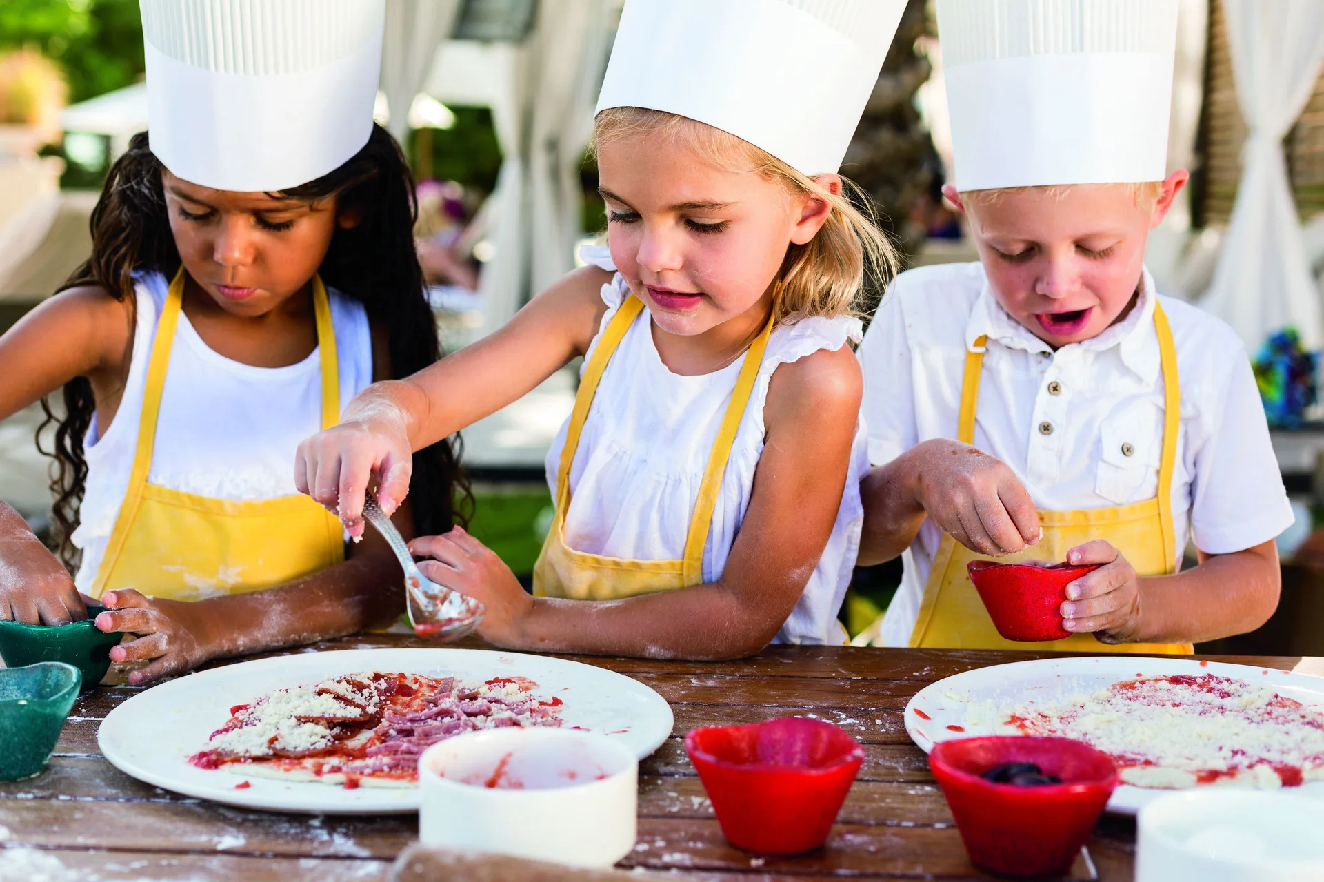 Children in chef hats decorate food outdoors at The Ritz-Carlton, Grand Cayman.