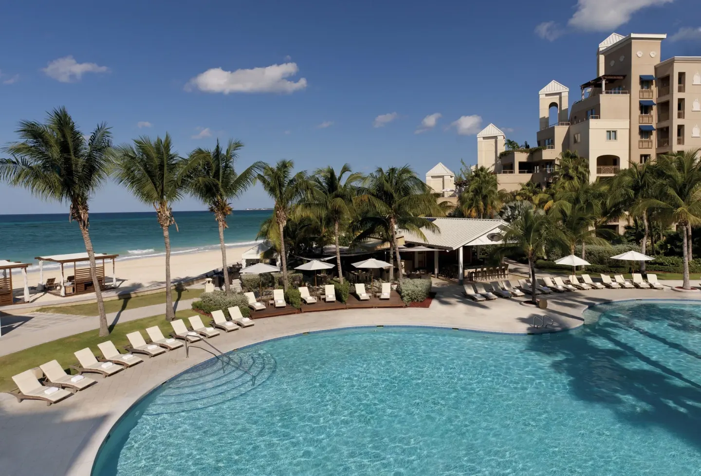 Oceanfront pool deck and beach beside palms at The Ritz-Carlton, Grand Cayman.