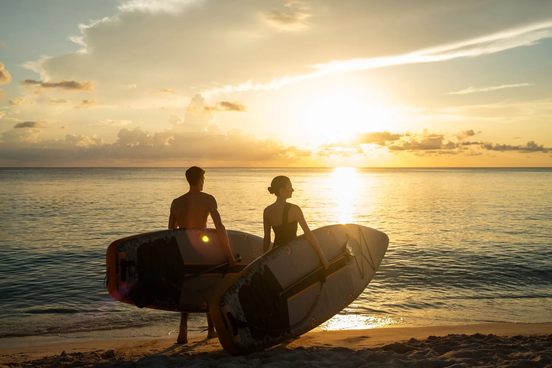 Two paddleboarders stand on the beach at sunset at The Ritz-Carlton, Grand Cayman.