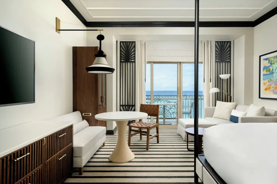 Oceanfront room sitting area and balcony beside a king bed at The Ritz-Carlton, Grand Cayman.