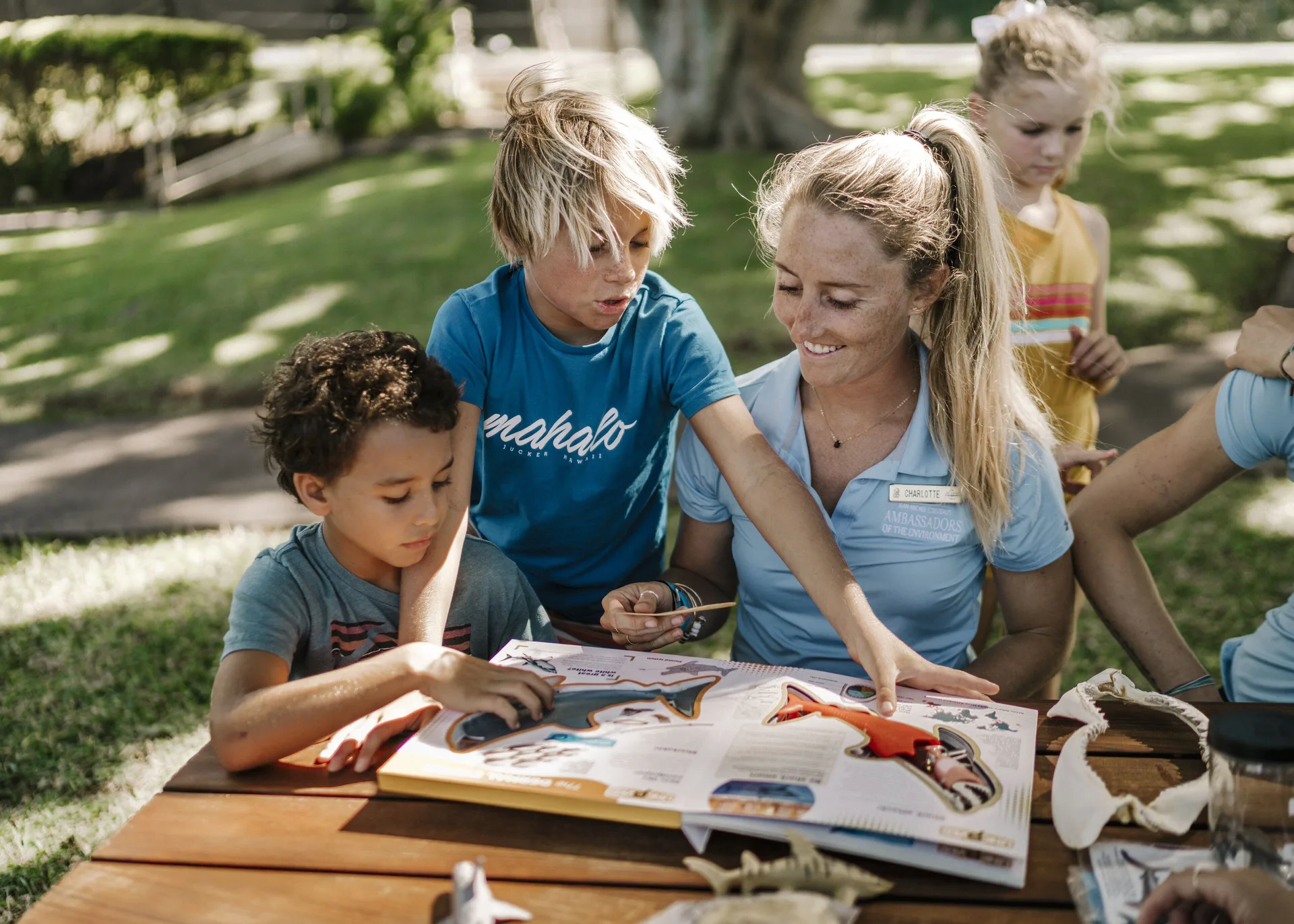 Children look at an activity book with a staff member at The Ritz-Carlton Maui, Kapalua.