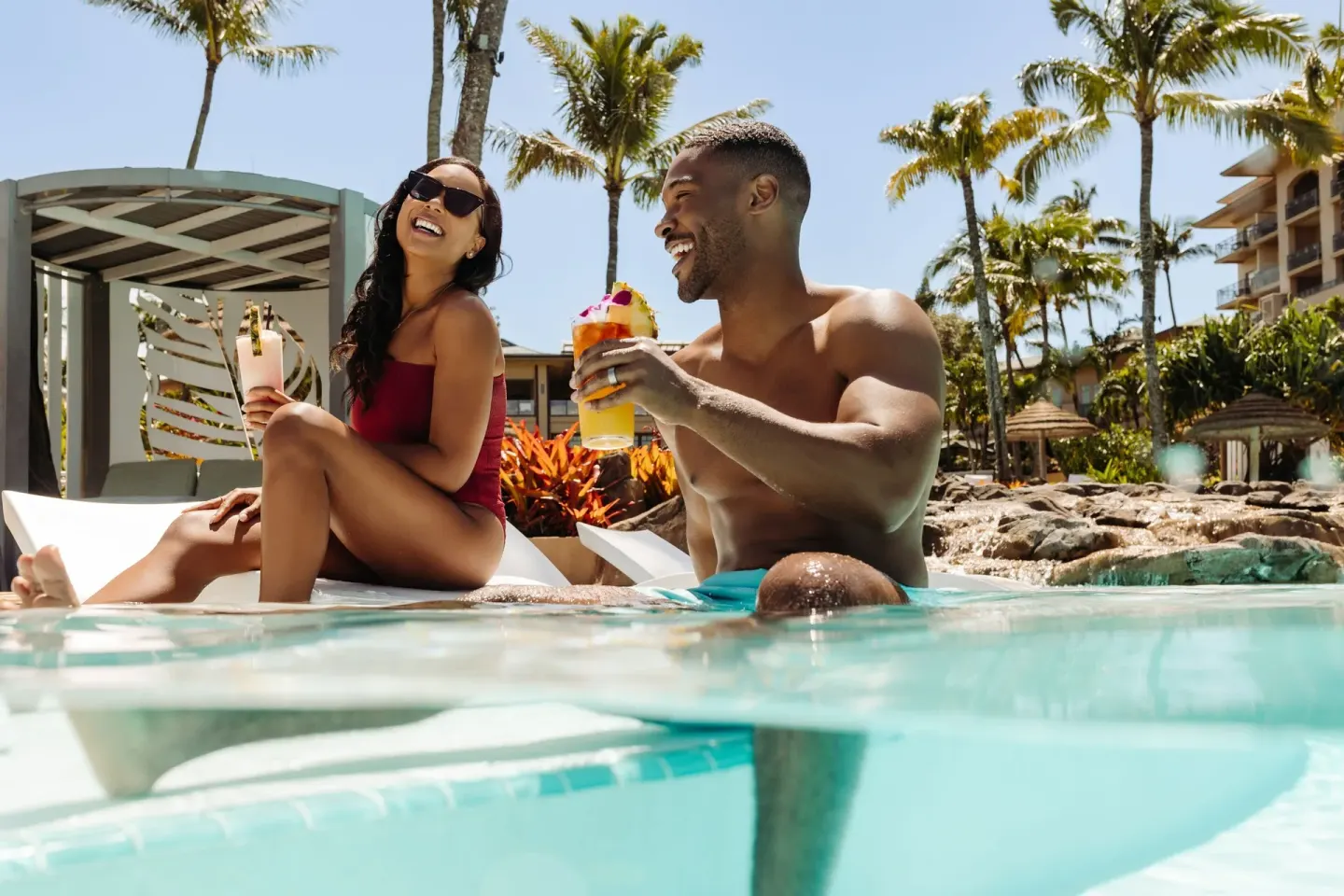 Couple holding tropical drinks in the resort pool at The Ritz-Carlton Maui, Kapalua.