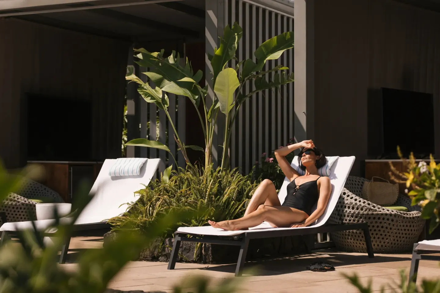 Guest sunbathing on a lounge chair by tropical landscaping at The Ritz-Carlton Maui, Kapalua.