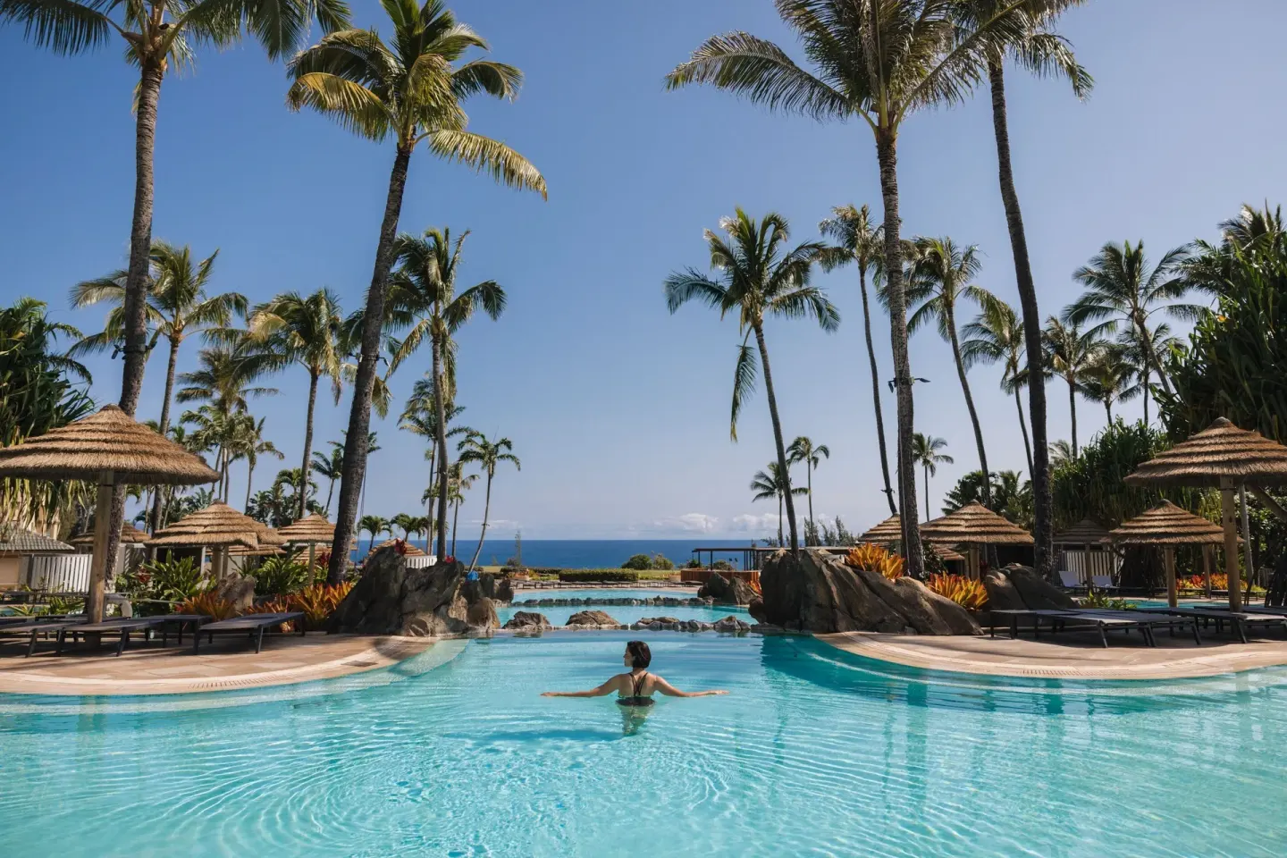 Resort pool with palm trees, cabanas, and ocean beyond at The Ritz-Carlton Maui, Kapalua.