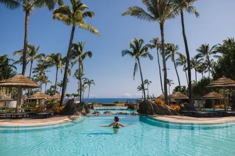 Resort pool with palm trees, cabanas, and ocean beyond at The Ritz-Carlton Maui, Kapalua.
