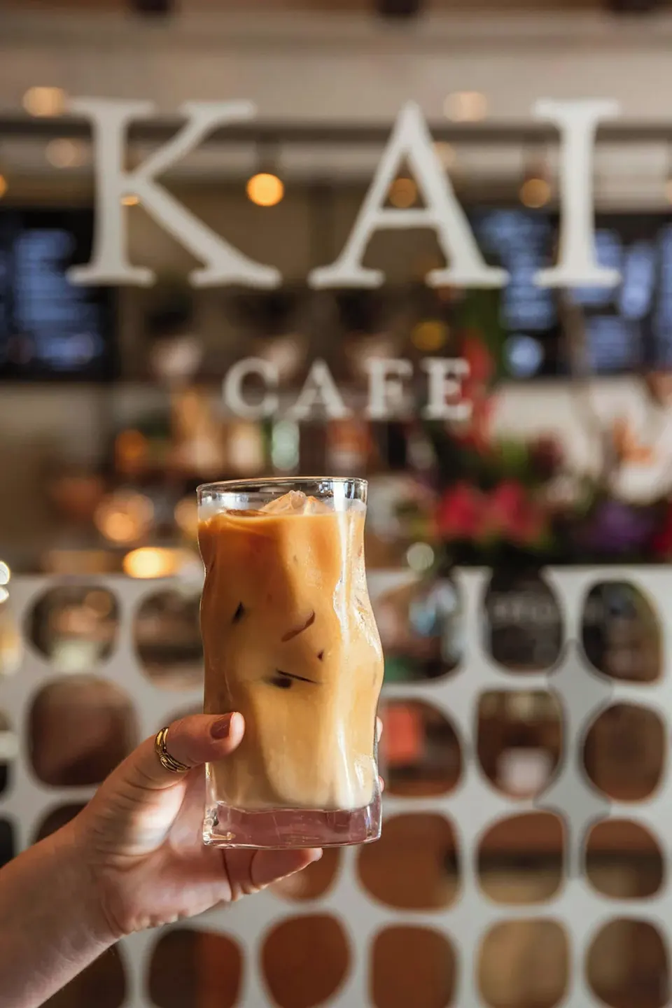 An iced coffee is held in front of the Kai Cafe sign at The Ritz-Carlton Maui, Kapalua.