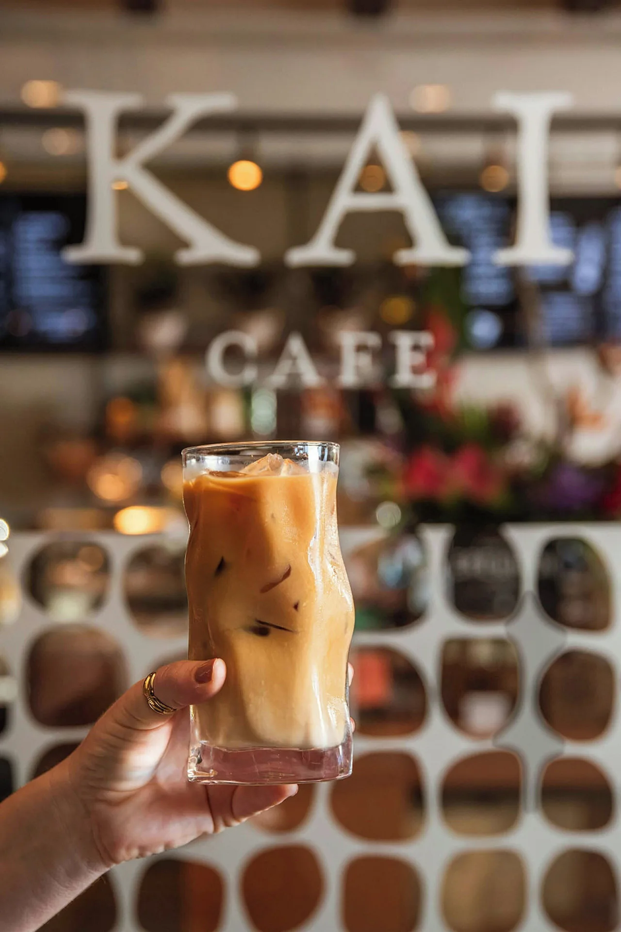 An iced coffee is held in front of the Kai Cafe sign at The Ritz-Carlton Maui, Kapalua.