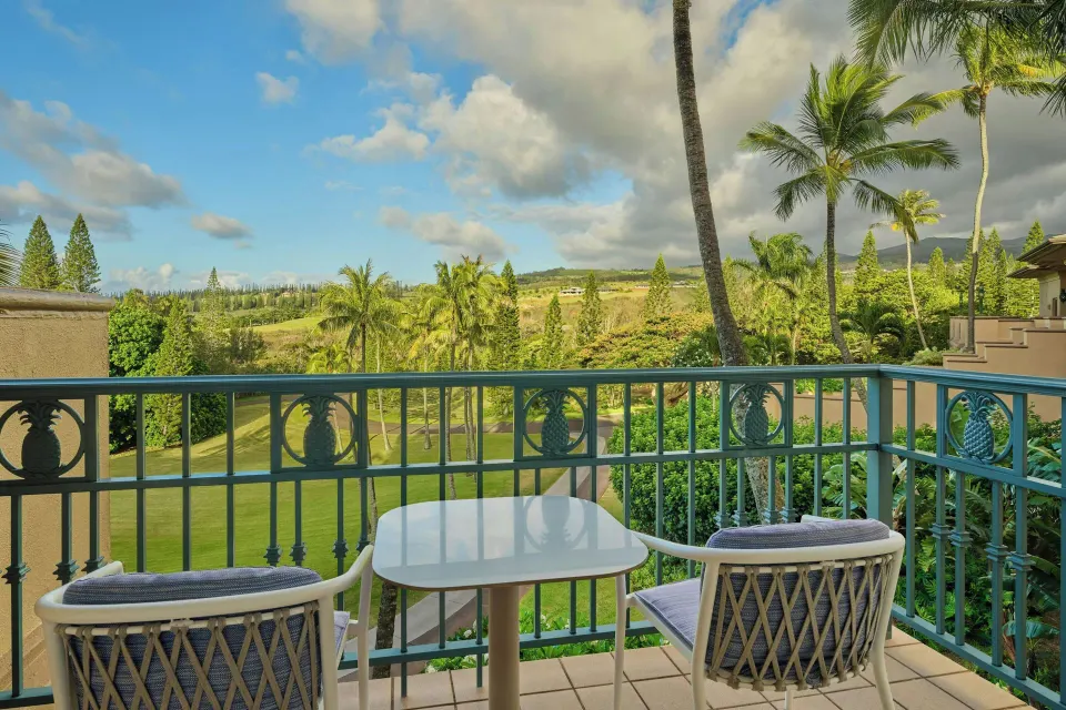Balcony table and chairs overlooking palms and lawns at The Ritz-Carlton Maui, Kapalua.