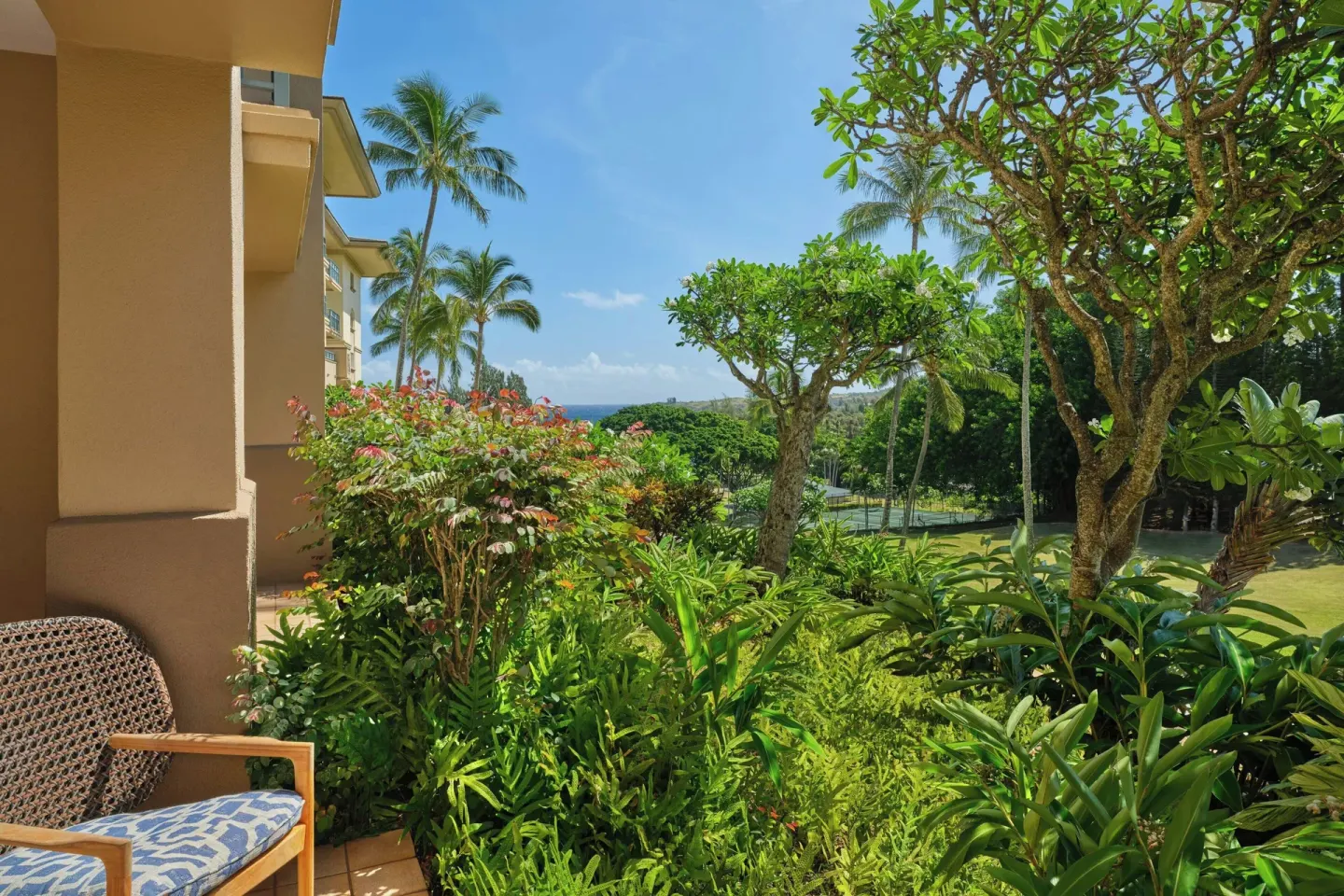 Garden patio view with palms and a glimpse of ocean at The Ritz-Carlton Maui, Kapalua.