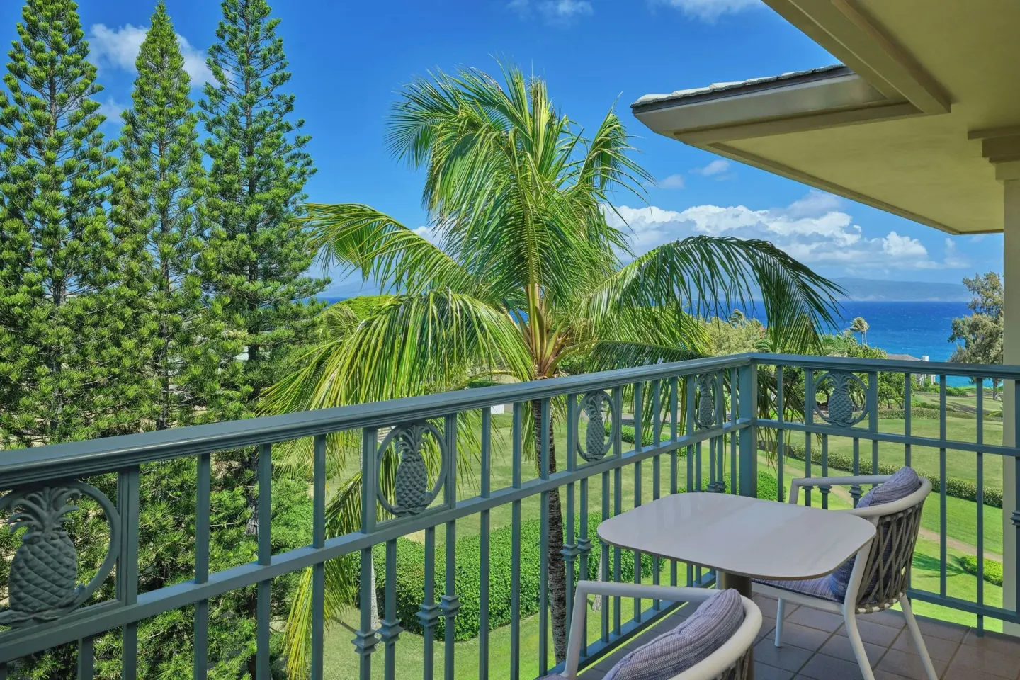 Deluxe Room partial ocean view balcony at The Ritz-Carlton Maui, Kapalua with table, chairs, and palms.