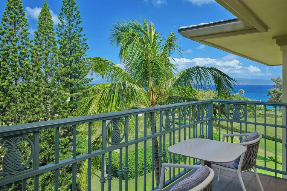 Deluxe Room partial ocean view balcony at The Ritz-Carlton Maui, Kapalua with table, chairs, and palms.