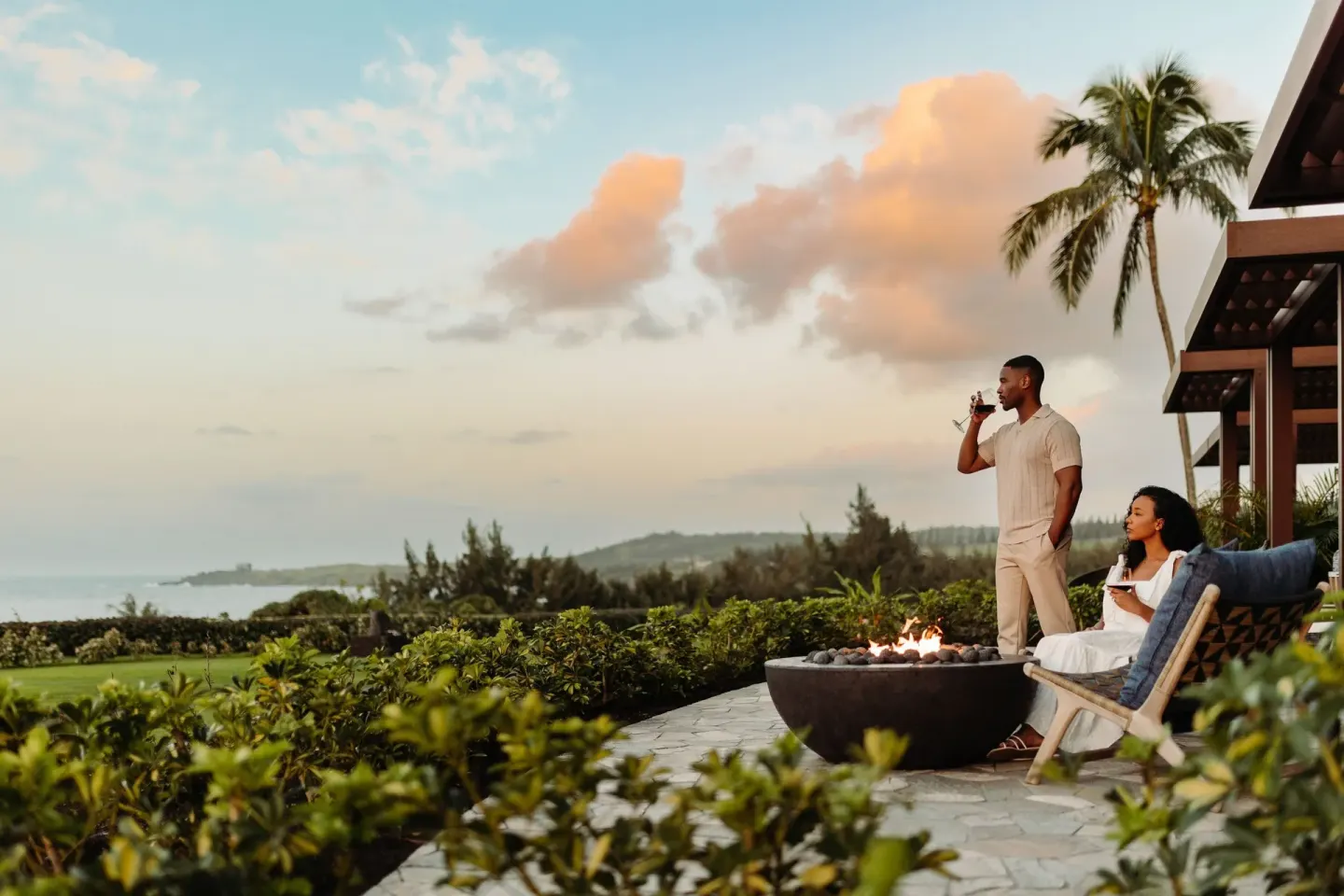 Fire Lanai terrace with guests, fire pit, palms and ocean at The Ritz-Carlton Maui, Kapalua.