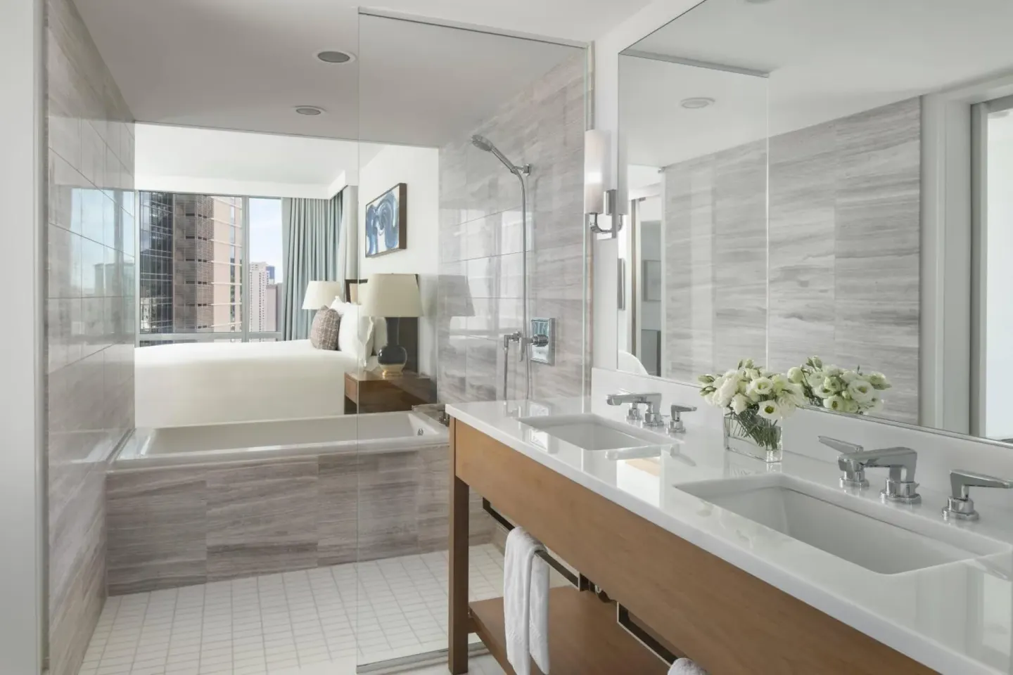 Bathroom at The Ritz-Carlton Residences, Waikiki Beach with double sinks, glass shower and bedroom view.