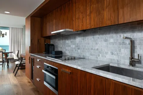 Suite kitchenette with wood cabinetry and gray tile backsplash at The Ritz-Carlton Residences, Waikiki Beach.