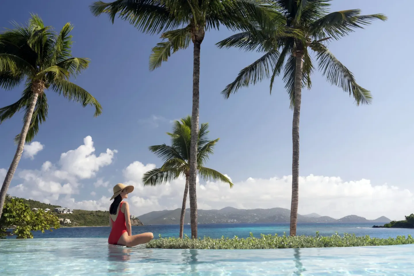 Guest sitting in an infinity pool with palms and bay views at The Ritz-Carlton, St. Thomas.