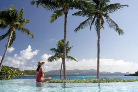 Guest sitting in an infinity pool with palms and bay views at The Ritz-Carlton, St. Thomas.
