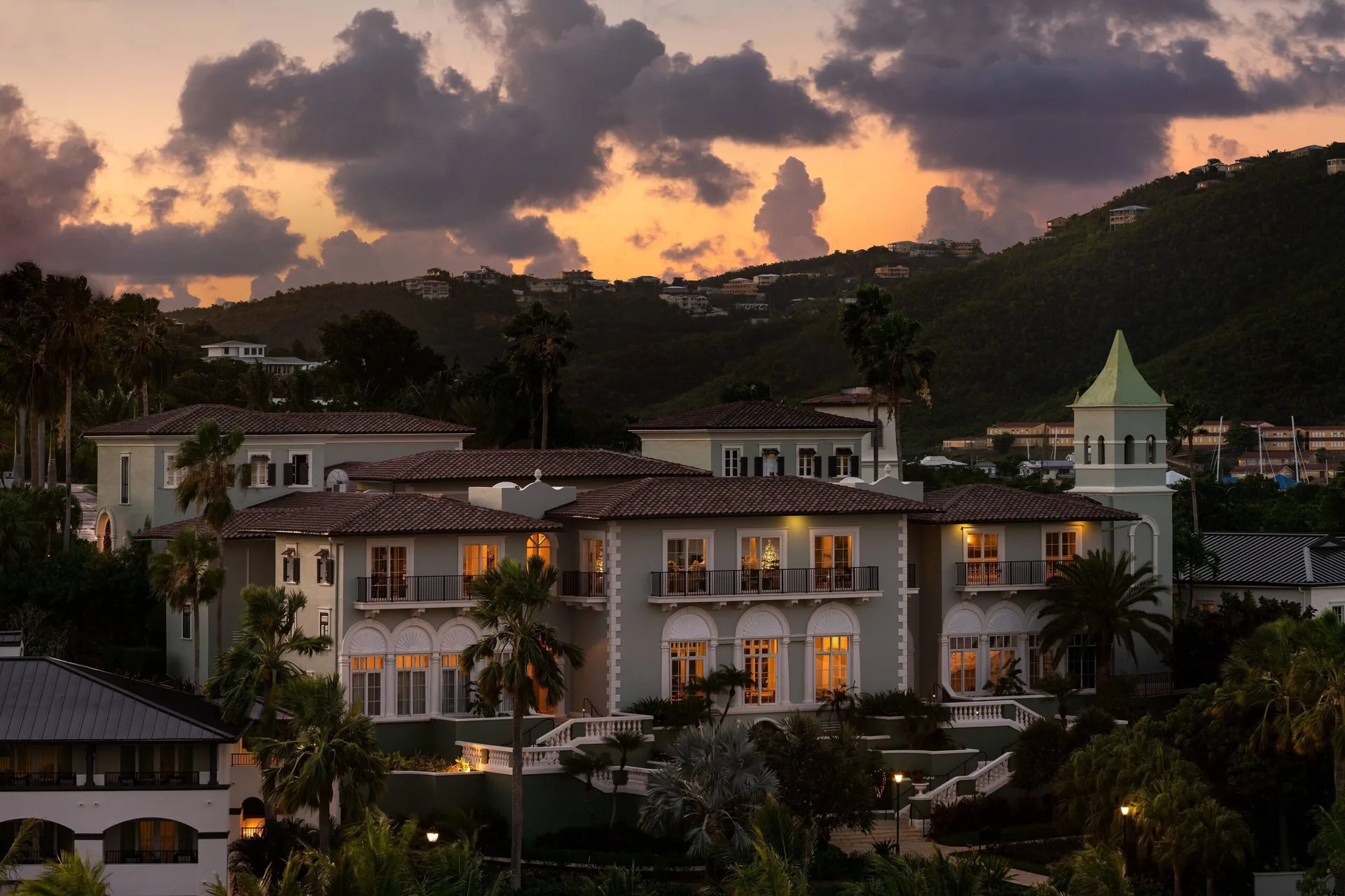 Resort buildings glow at sunset at The Ritz-Carlton, St. Thomas, with green hills behind them.